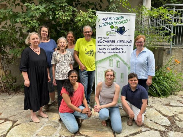 Das Foto zeigt das Büchereiteam im Garten des Hauses im Grünen mit dem Bücherei-Roll-up.